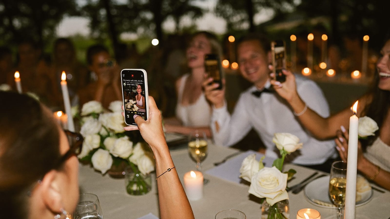 Invitați la masa de nuntă fotografiind petrecerea cu telefoanele, în lumină caldă de seară